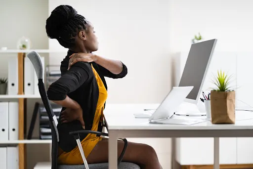 Employee experiencing neck and back pain at her desk, highlighting the need for prevention in workforce health strategies